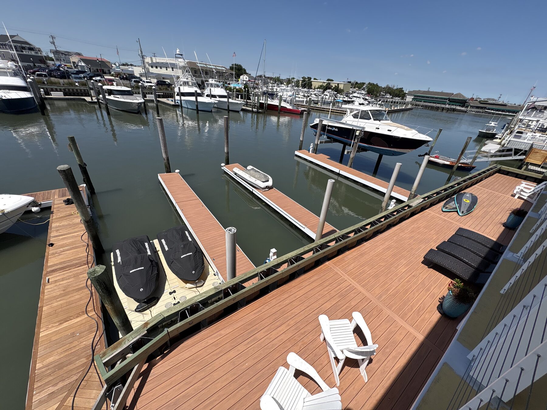 View from the Yacht Avenue floating dock — boat slips, jet skis on a lift, paddle board, and Adirondack chairs overlooking the Cape May marina